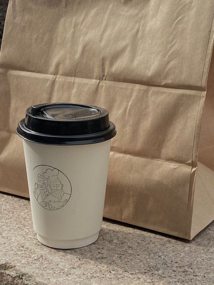 a coffee cup sitting on top of a counter next to a brown bag