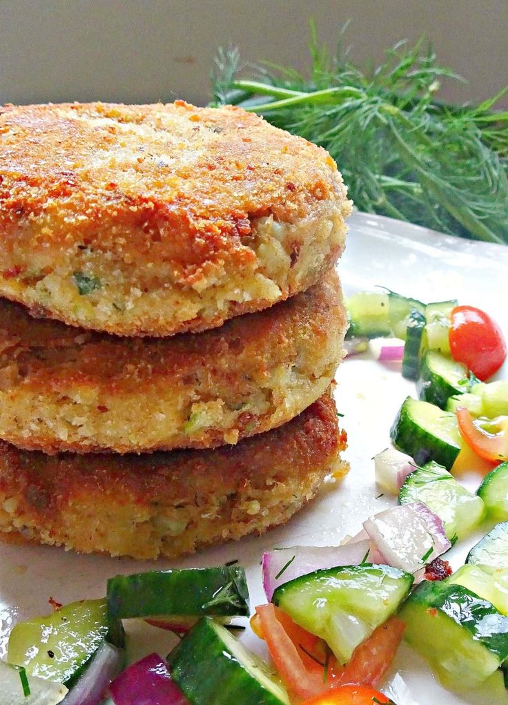 two crab cakes are stacked on top of each other next to a pile of vegetables