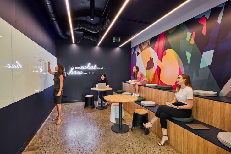 people are sitting at tables and talking in an office with colorful wallpaper on the walls