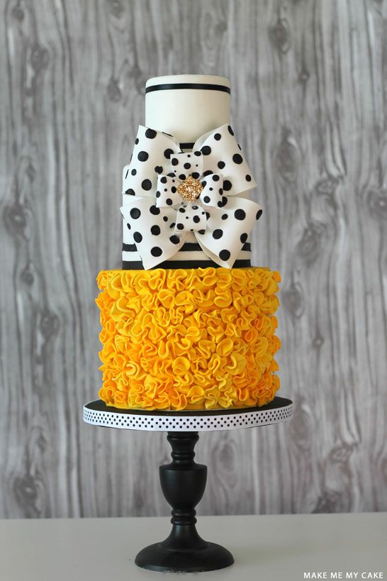 a three tiered cake decorated with black and white polka dots, yellow ruffles and a bow