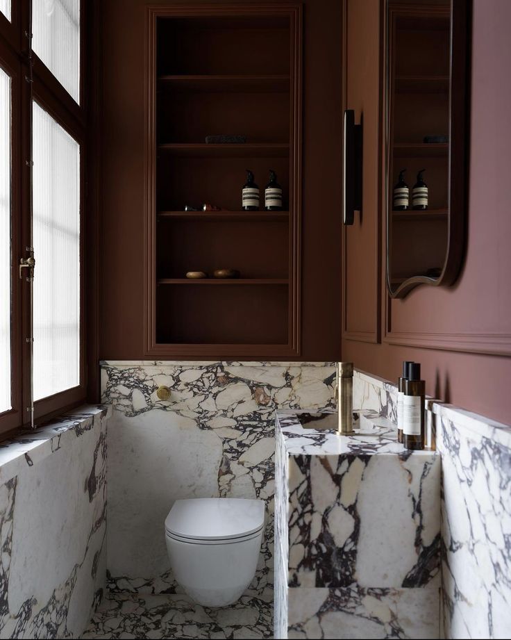 a white toilet sitting inside of a bathroom next to a sink and window with brown trim