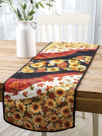 a table runner with sunflowers on it and a vase full of flowers in the background