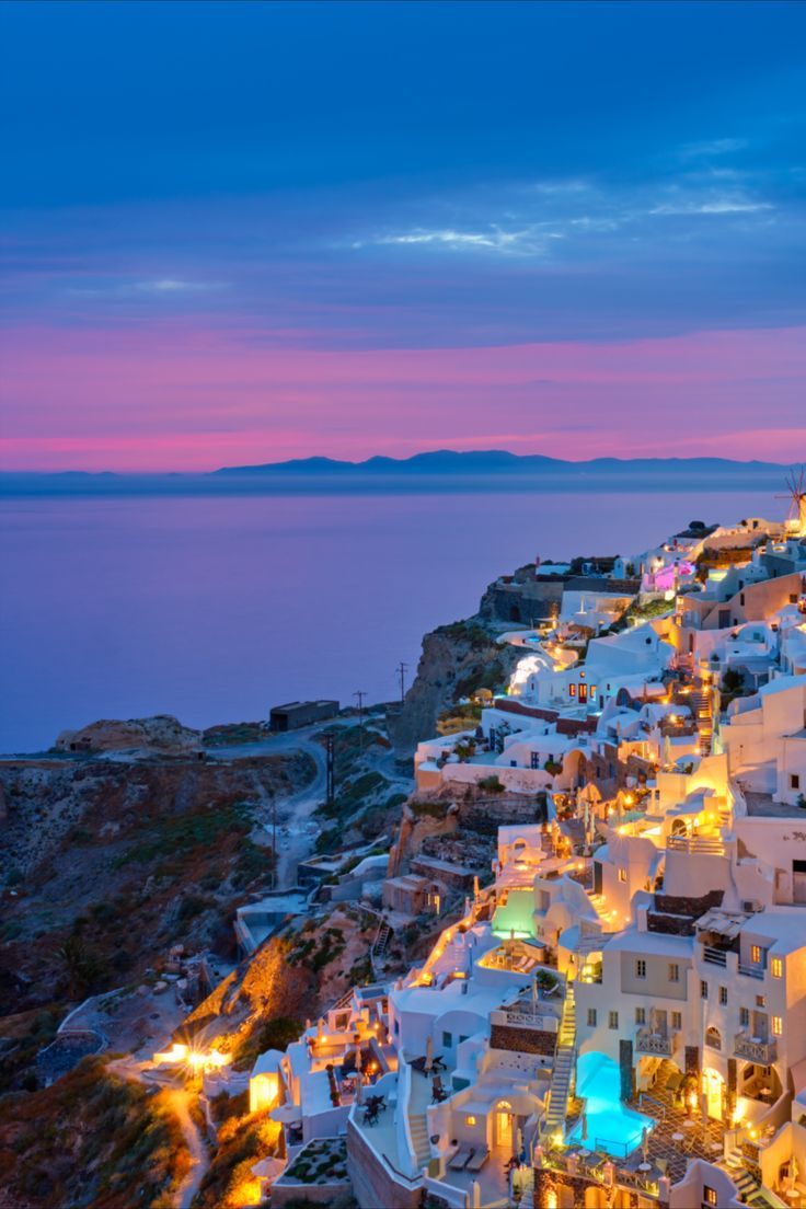 the town is lit up at night by the ocean