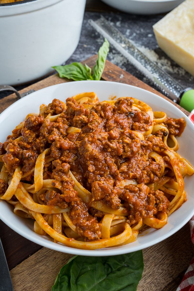 a white bowl filled with pasta and meat sauce on top of a wooden cutting board