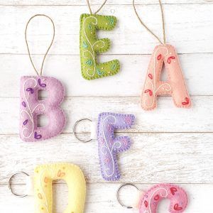 four felt letters hanging from strings on a white wooden surface with the letter e, f, and c