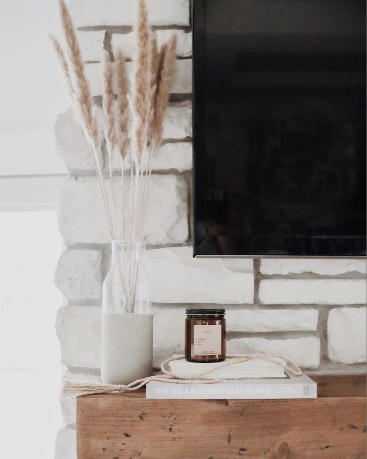 a tv mounted on a brick wall next to a vase with dry grass in it