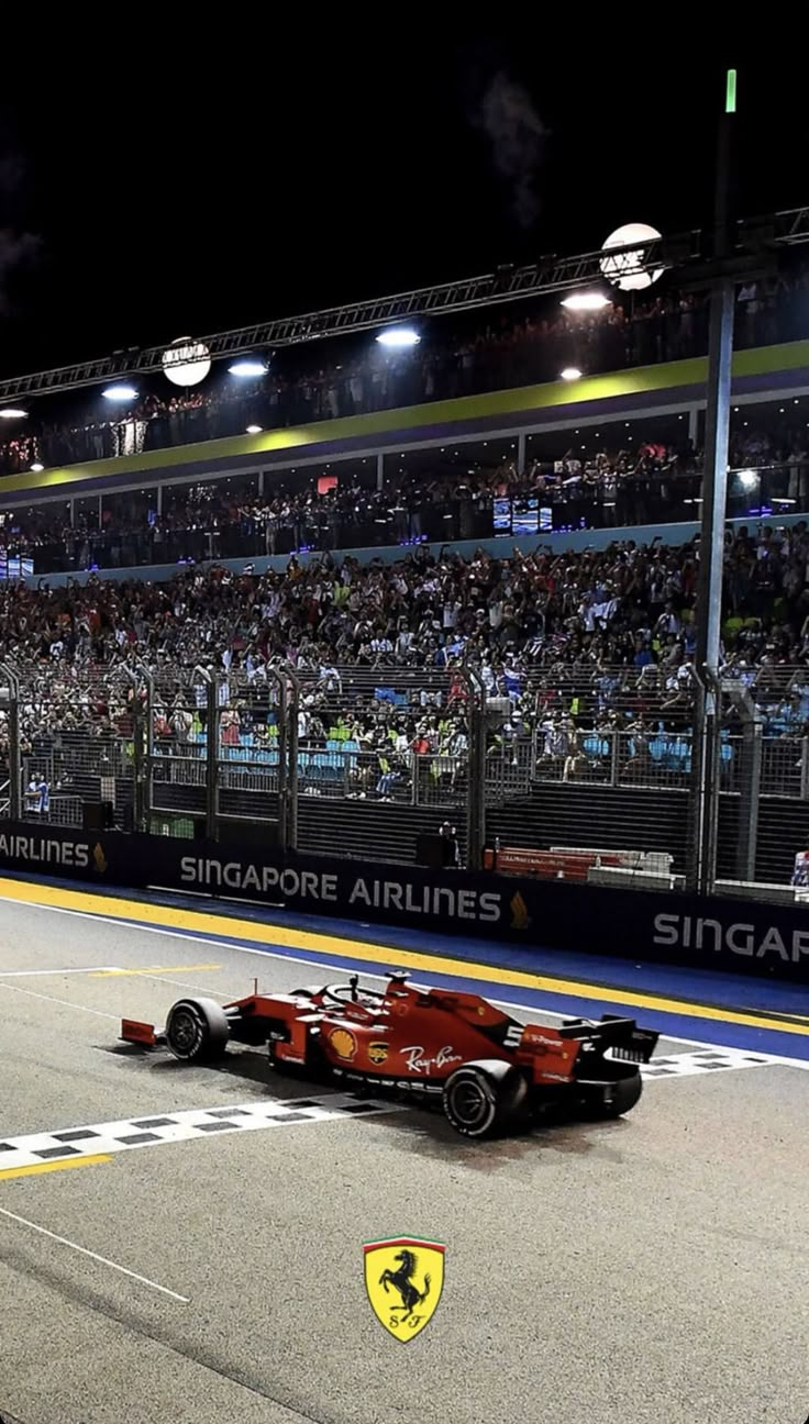 a red race car driving down the track in front of an audience at night time