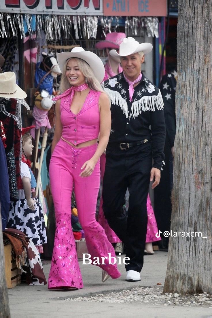 two women in pink outfits are walking down the street with cowboy hats on their heads