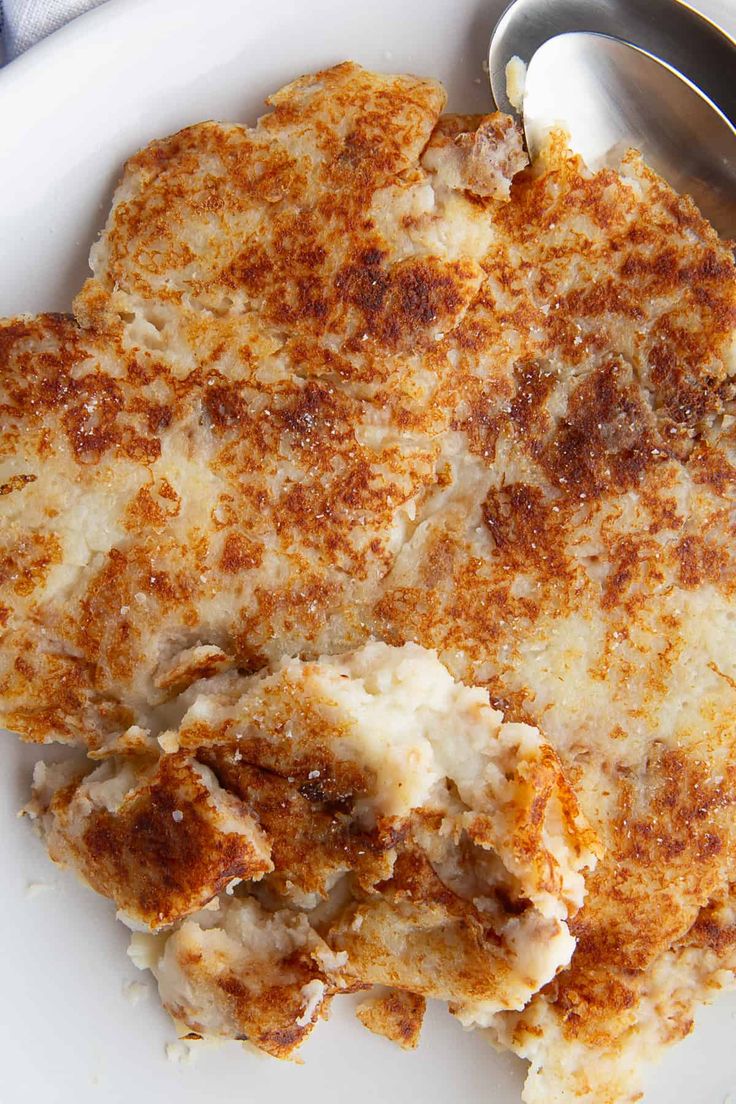 a close up of a plate of food with meat and cheese on it, next to a spoon