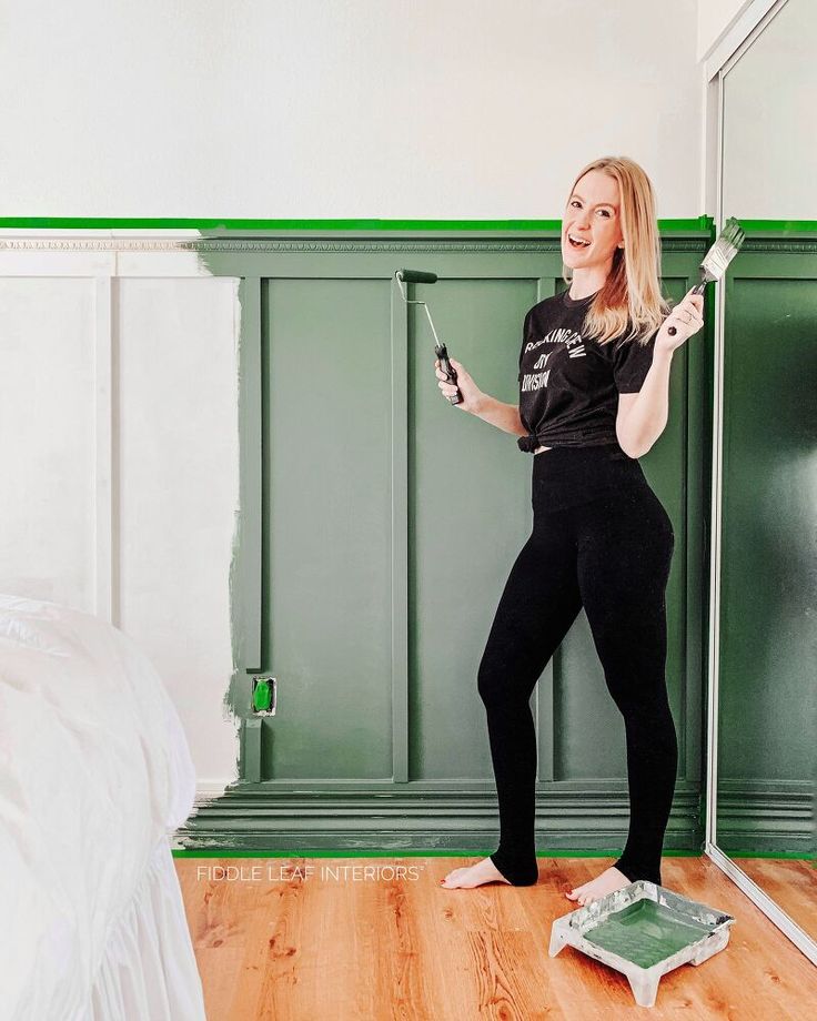 a woman standing in front of a mirror holding a paint roller and painting the walls