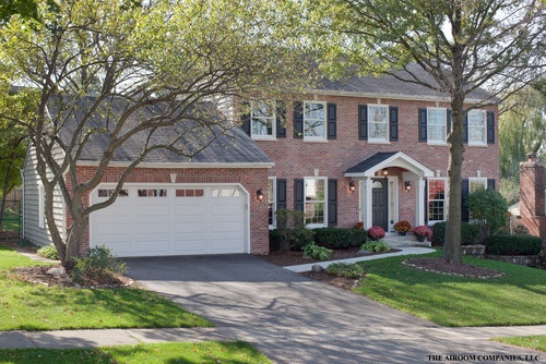 a large brick house with two garages and trees in front of the house on a sunny day