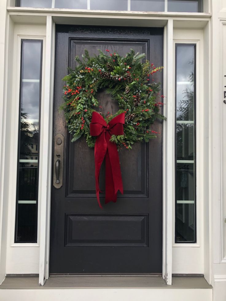 a wreath on the front door of a house with a red bow hanging from it