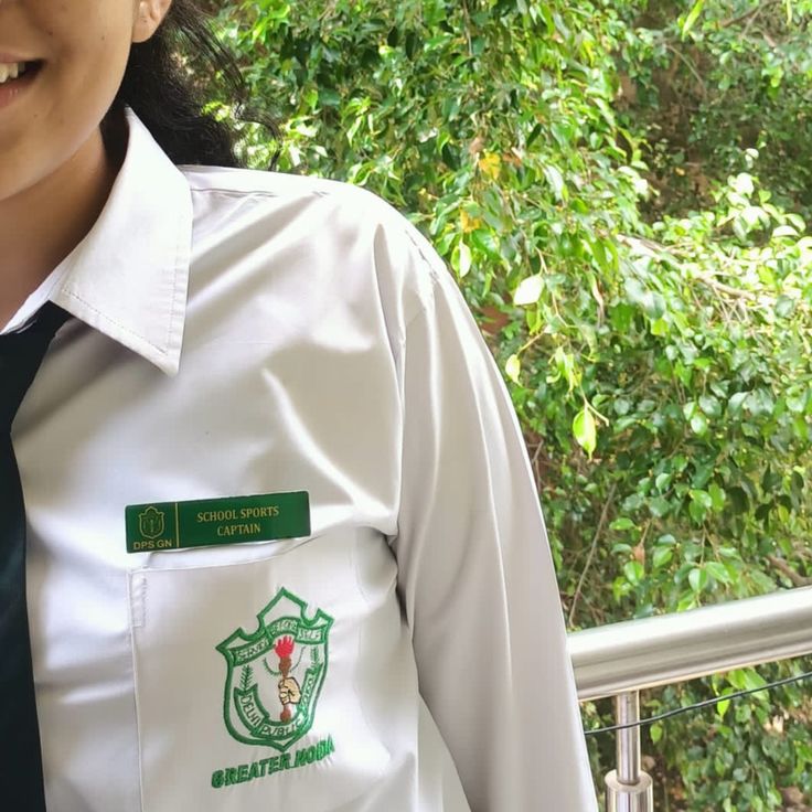 a woman wearing a white shirt and black tie standing in front of some green trees