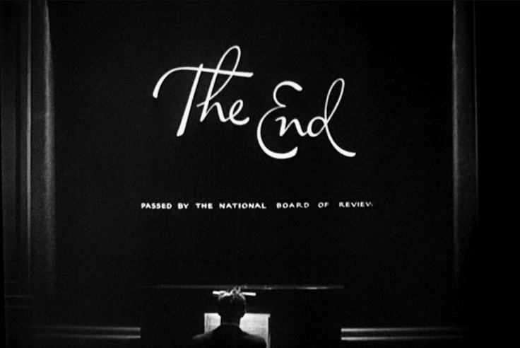 black and white photograph of the end sign in front of a dark room with light coming through it