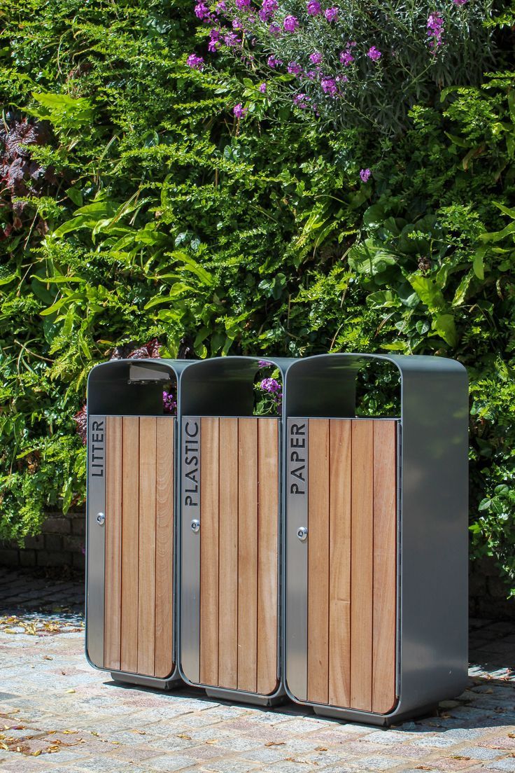 three trash cans sitting next to each other in front of some bushes and purple flowers