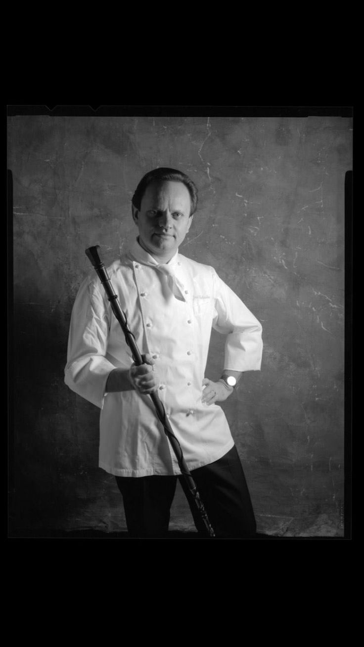 a black and white photo of a man in chef's coat holding a baseball bat