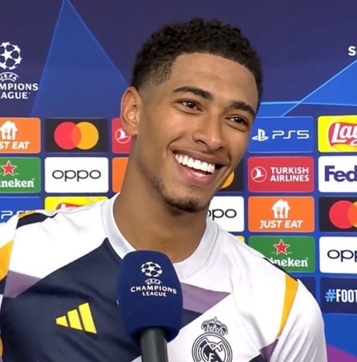 the soccer player is smiling while holding a microphone in front of him and talking to the media