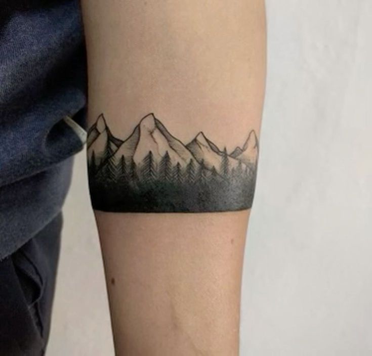 a person with a tattoo on their arm that has mountains and trees in the background