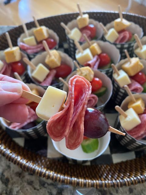 a person holding a skewer of meat and cheese on a stick with olives