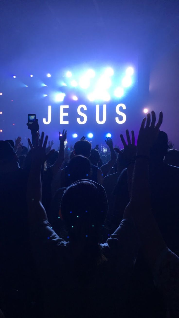 people are holding their hands up in front of a stage with lights and the words jesus on it