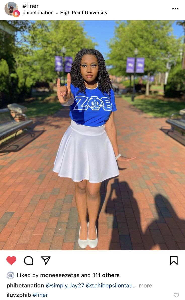 a woman in a blue shirt and white skirt is standing on a brick walkway with her hand up