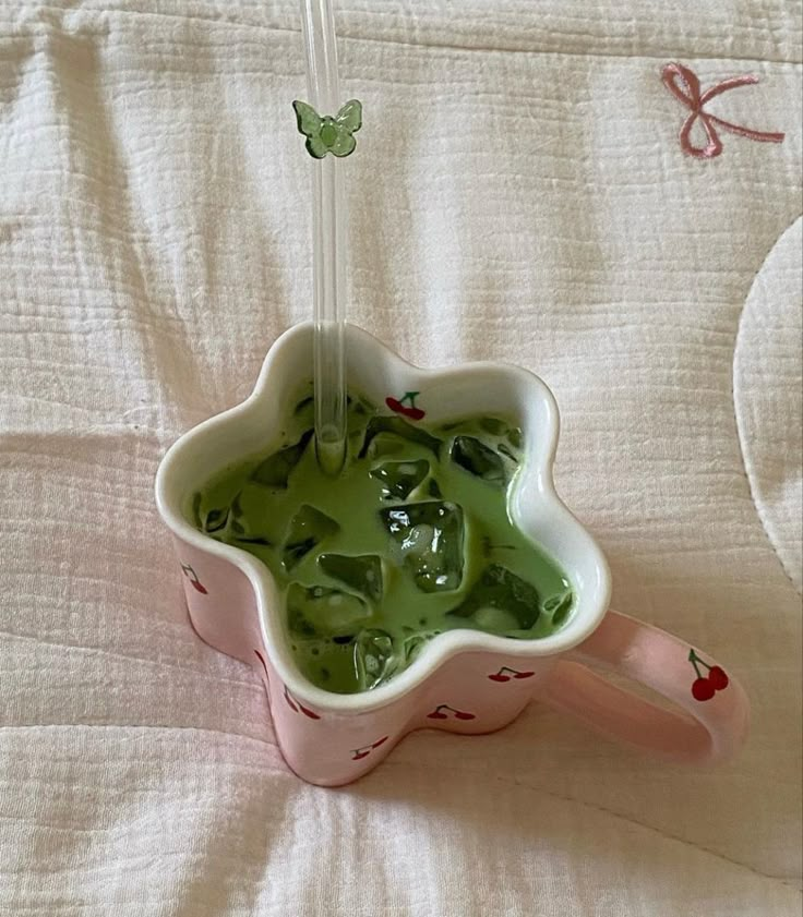 a cup filled with green liquid sitting on top of a white bed covered in butterflies