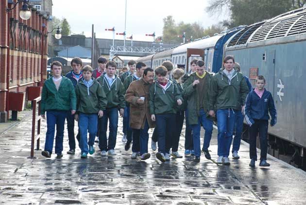 a group of people walking down a sidewalk next to a train