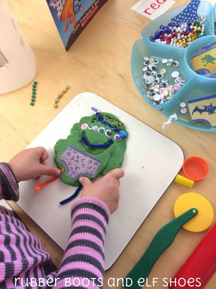 a child is decorating a green monster cookie on a cutting board with scissors and beads