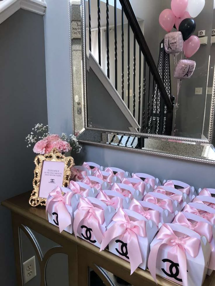 a table topped with lots of pink and white gift bags next to a stair case