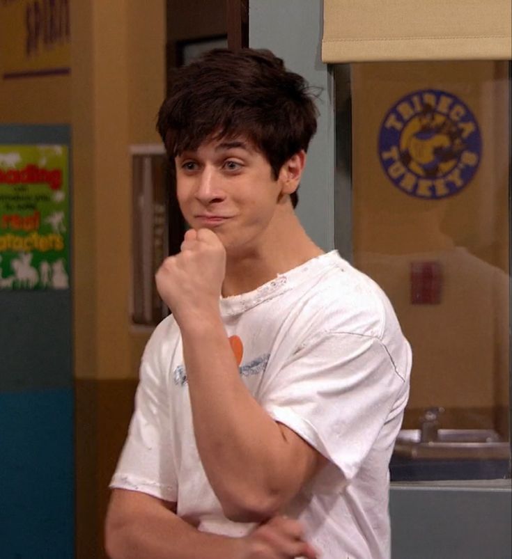 a young man standing in front of a door with his hand on his chin and looking at the camera