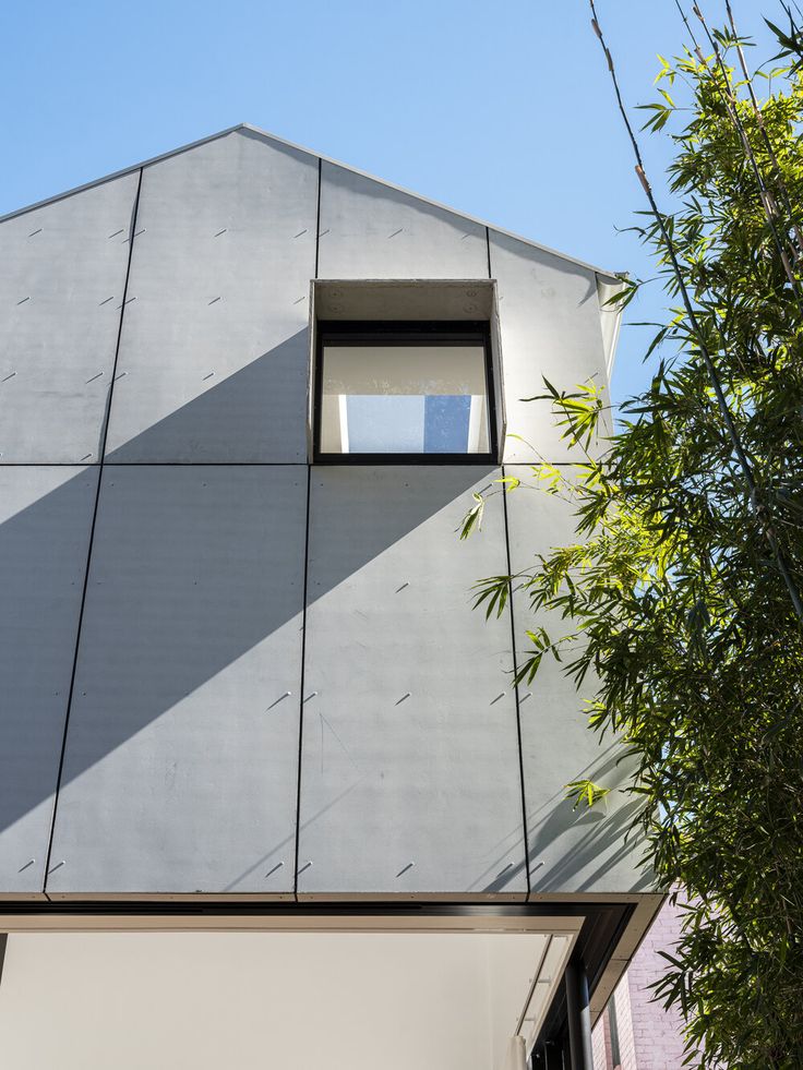 the corner of a building with a window on it's side and a tree next to it