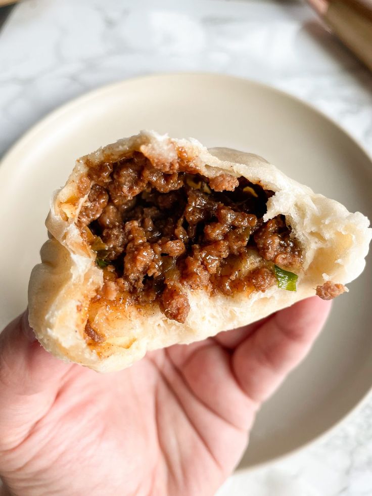 a hand holding up a piece of food with meat and vegetables in it on a white plate