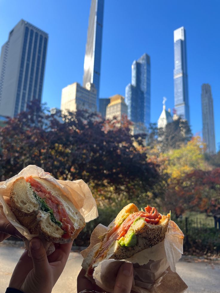 two hands holding sandwiches in front of a city skyline