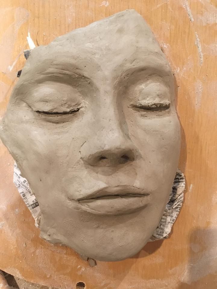 a clay face sitting on top of a piece of wood