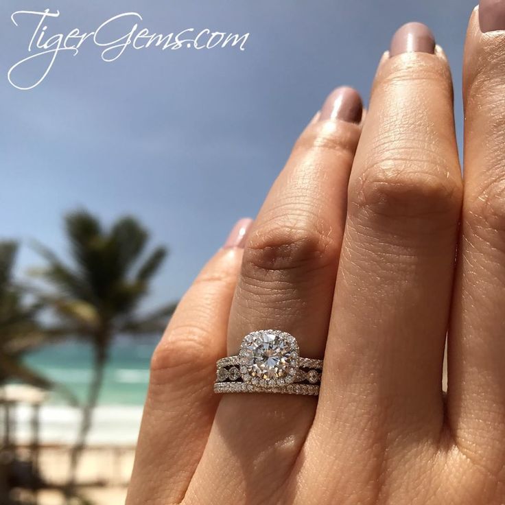 a woman's hand with a diamond ring on it and the ocean in the background