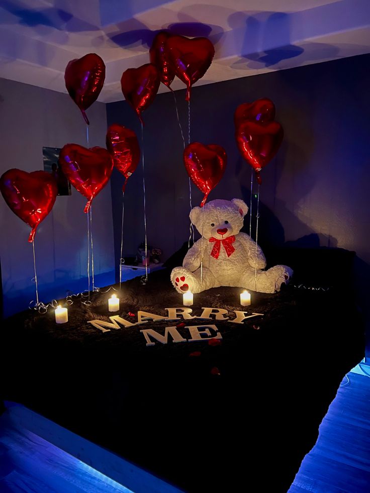 a teddy bear sitting on top of a bed surrounded by candles and heart shaped balloons