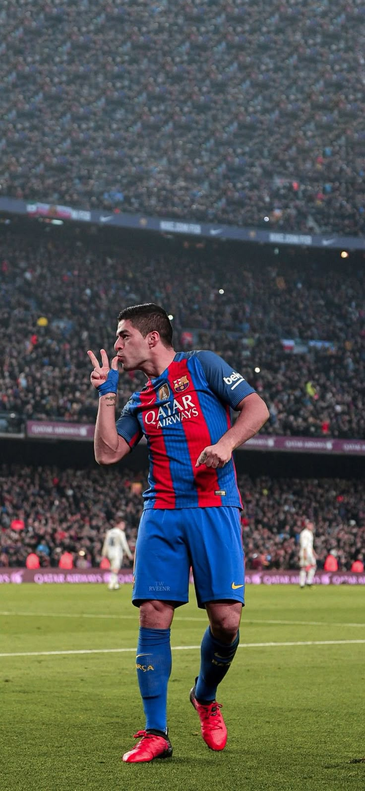 a soccer player standing on the field with his hand up to his mouth and people in the stands behind him