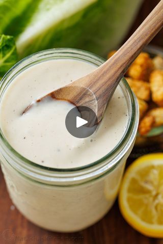 a wooden spoon in a jar filled with white liquid next to lemons and lettuce