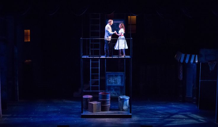 two people standing on top of a wooden platform in front of a dark room with blue lighting