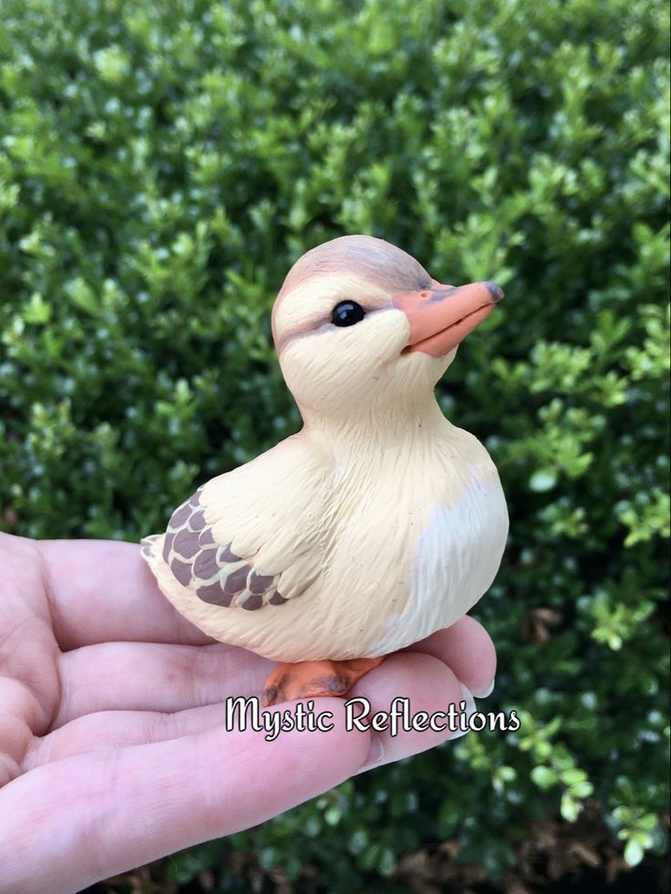 a small toy duck sitting on top of someone's hand in front of some bushes