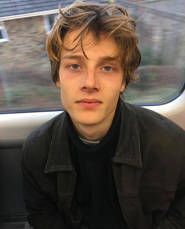 a young man is sitting on a train looking at the camera while wearing a black jacket