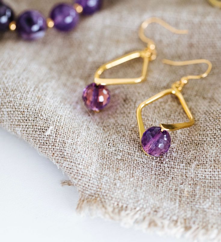 A faceted Amethyst bead set in a double sided diamond shaped frame creates demure drop earrings. 8mm faceted amethyst beadgold plated brass double sided diamond shaped bailgold plated brass french ear wires drop: 2"width: 3/4" Handmade in Lincoln, Nebraska Gold Teardrop Faceted Beads Jewelry, Gold Teardrop Jewelry With Faceted Beads, Faceted Amethyst Purple Jewelry, Faceted Purple Amethyst Jewelry, Purple Faceted Amethyst Jewelry, Faceted Purple Jewelry For Gifts, Faceted Purple Jewelry Gift, Purple Faceted Jewelry For Gift, Nickel-free Diamond-shaped Jewelry For Gifts