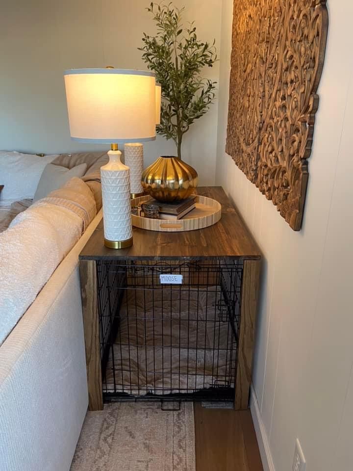 a dog crate sitting on top of a wooden table next to a white couch and lamp