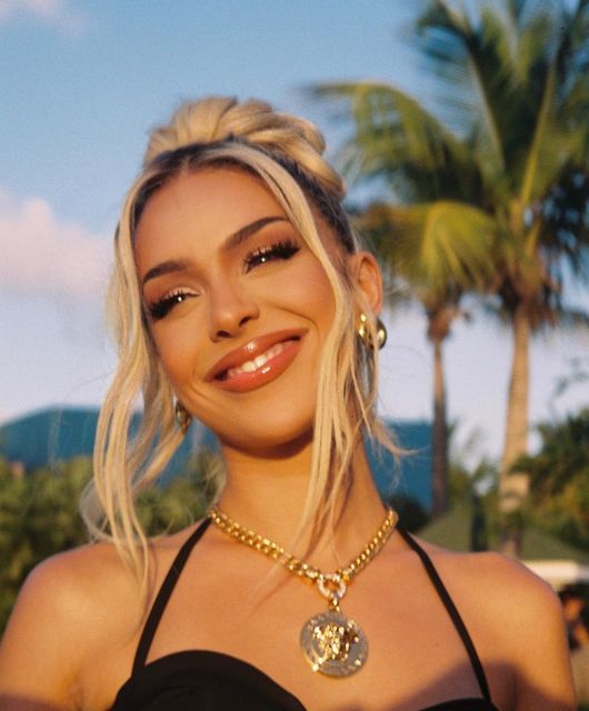 a woman with blonde hair wearing a black top and gold necklace smiling at the camera