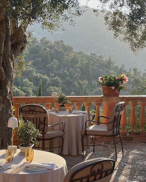 an outdoor dining area with tables and chairs, overlooking the hills in the distance is covered by white tablecloths