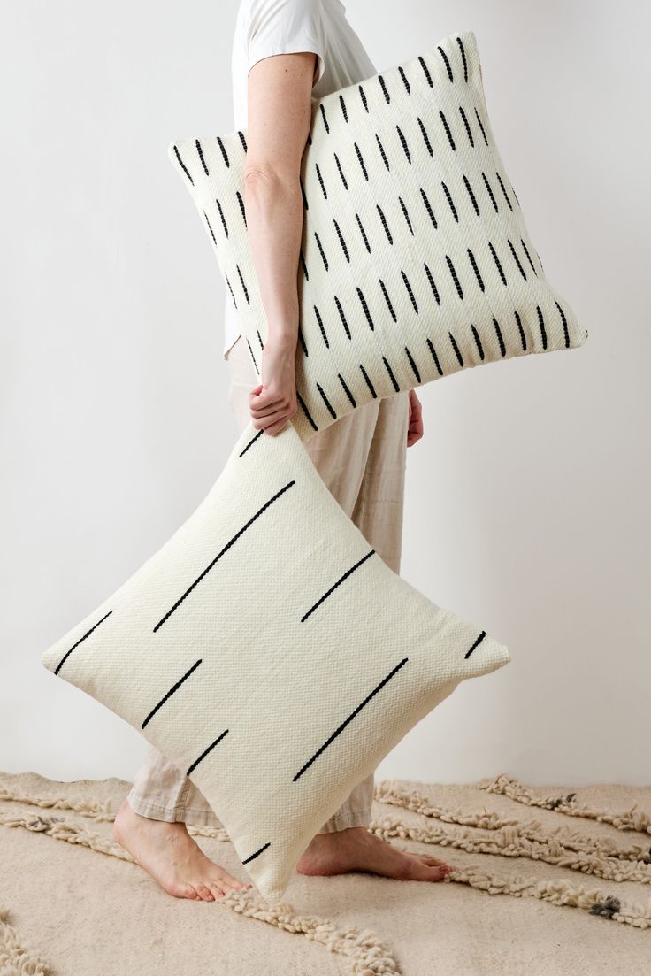 a woman holding two pillows in her hands while standing on the floor with it's back to the camera