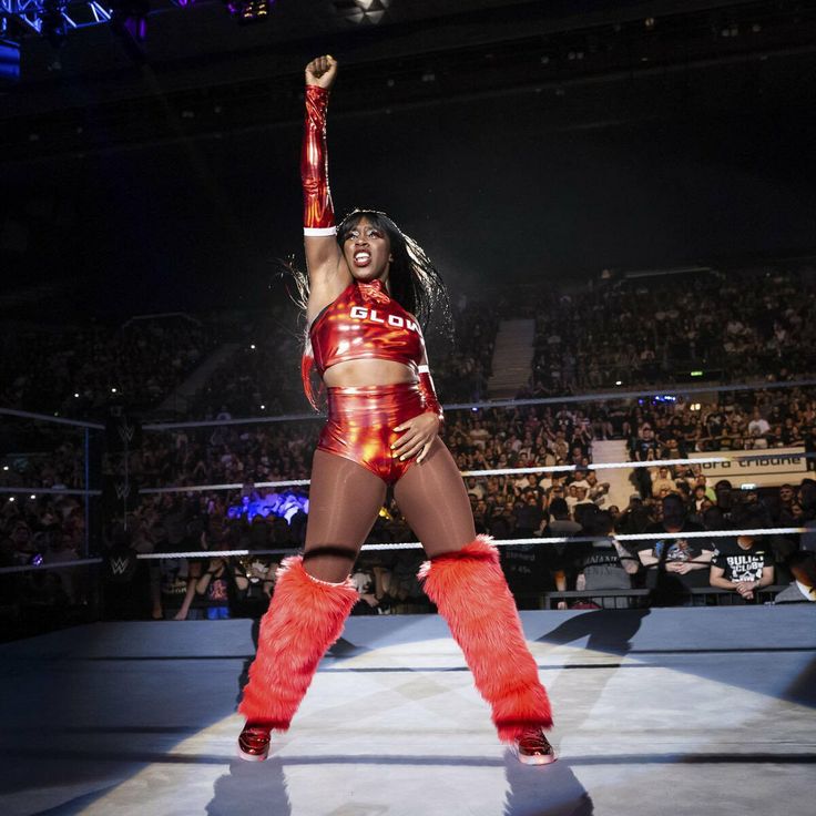 a woman in red and black outfit standing on top of a wrestling ring with her arms up