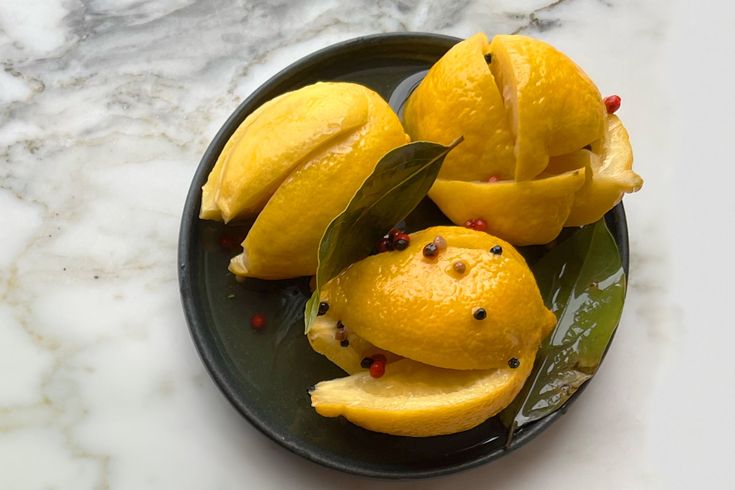 sliced lemons on a plate with leaves and pepper sprinkled around them sitting on a marble counter top