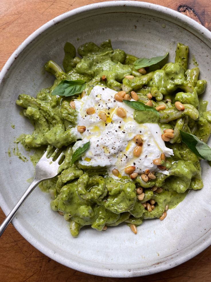 a white bowl filled with guacamole covered in sour cream and topped with pine nuts