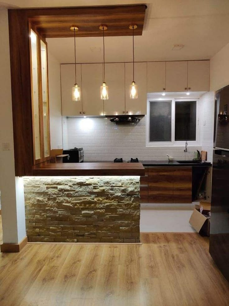 an empty kitchen with wooden floors and white walls, lights hanging from the ceiling over the counter